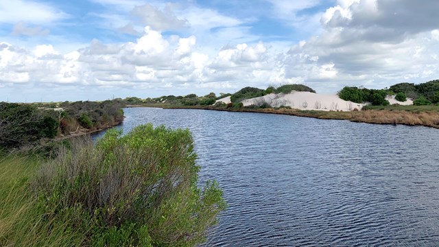 A remote island with sparse vegetation is seen from the water.