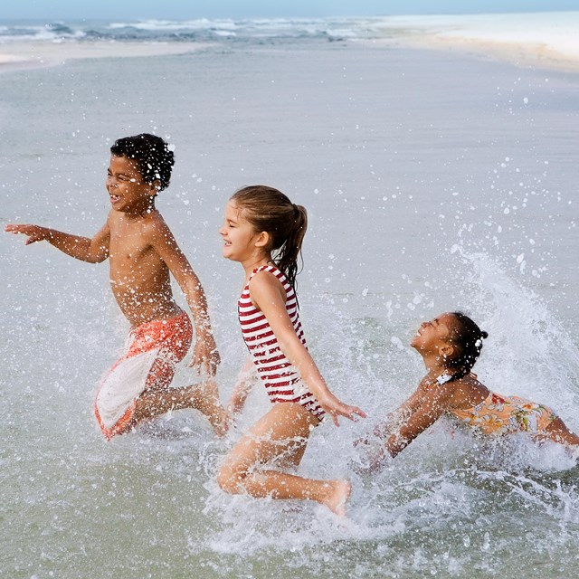 A group of children run through a tidal pool at the beach.
