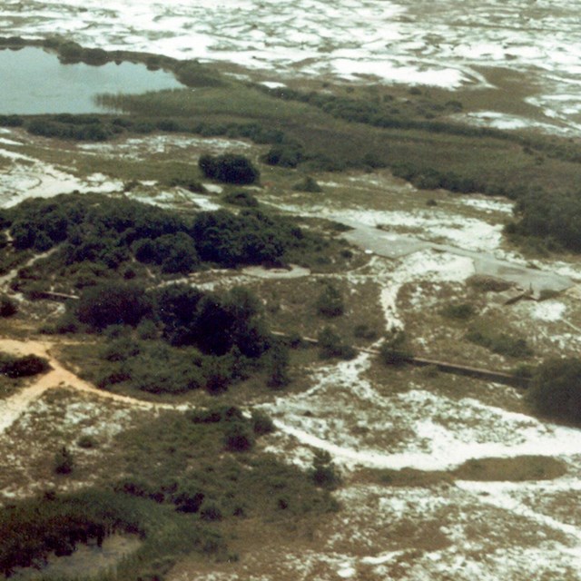 Aerial image of a barrier island with portions of three concrete structures visible.