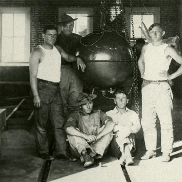 A black and white photo of four men standing around a suspended mine case.