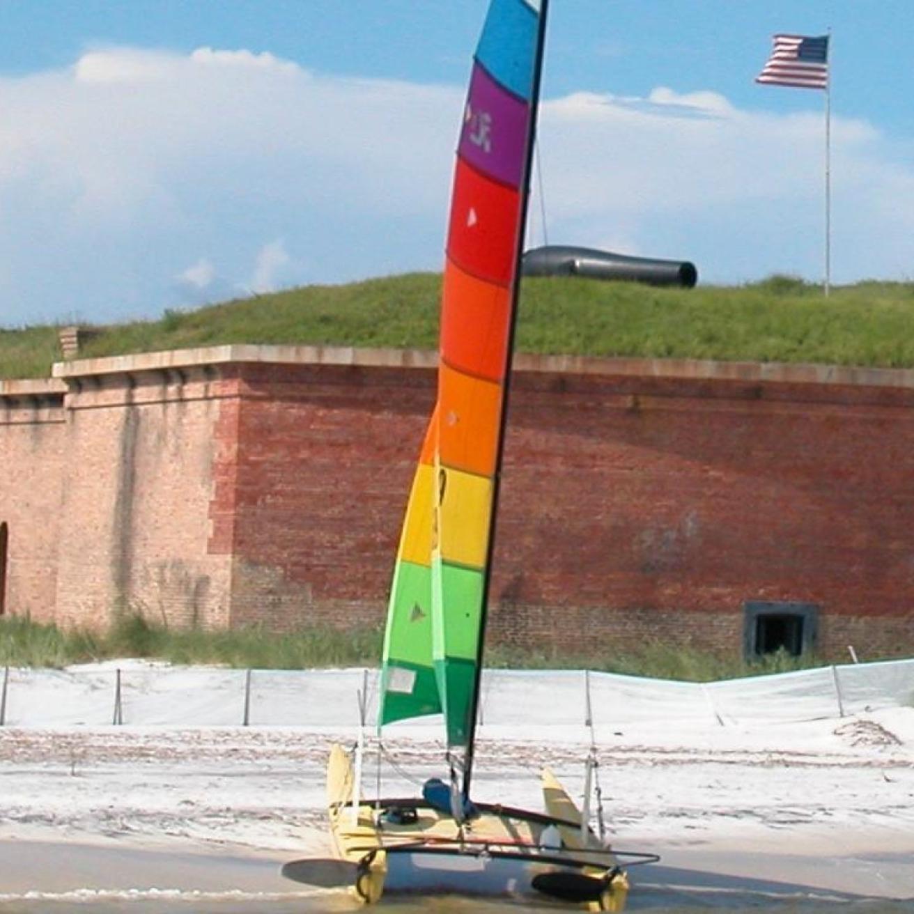 A colorful sailboat is beached in front of a large brick fort.