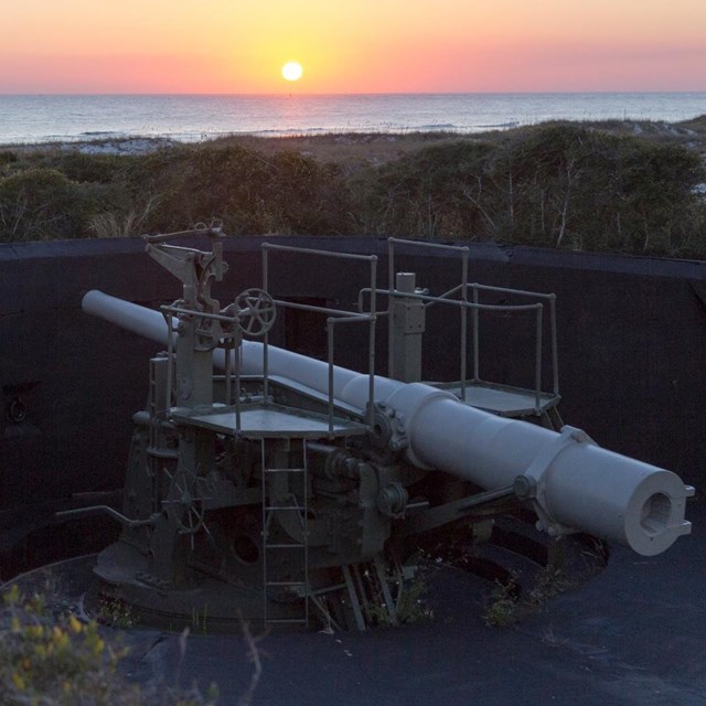 The sunsets over the water, in the foreground a cannon is mounted.