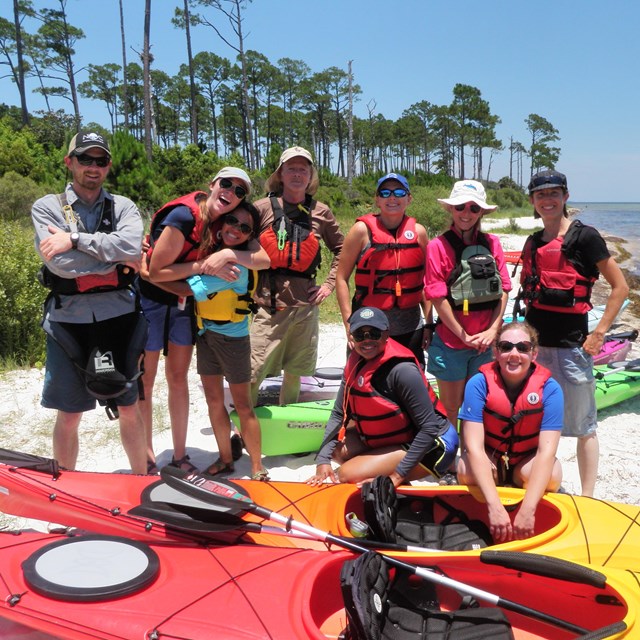 A group of people in life jackets stand around kayaks.
