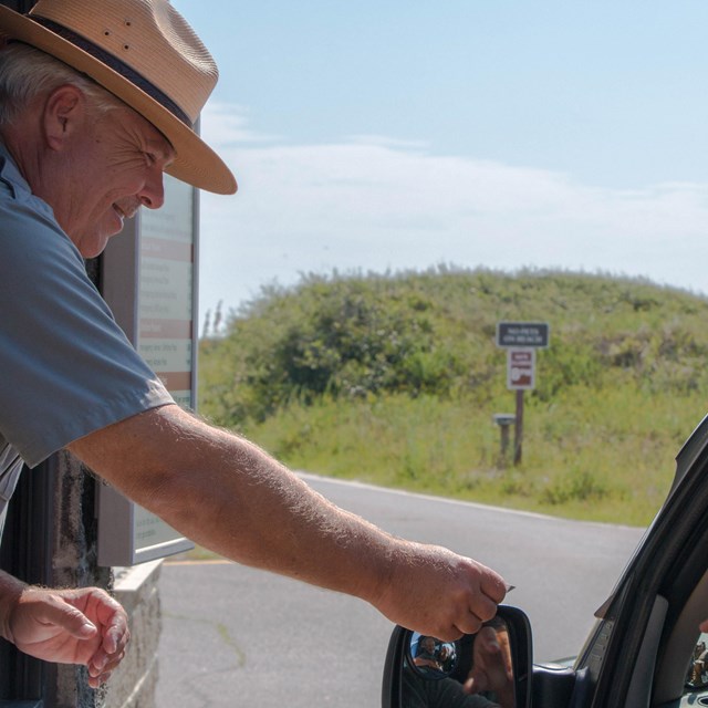 A ranger hands a pass back to a visitor in a vehicle.