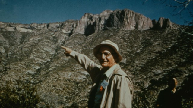 An old man points upward in a desert mountain canyon
