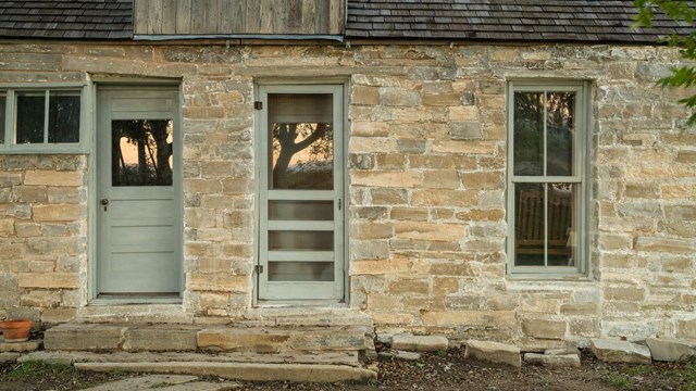 A stone wall with doors and windows forms the front of a ranch house