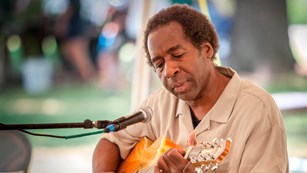 A man playing a guitar at a park special event. 