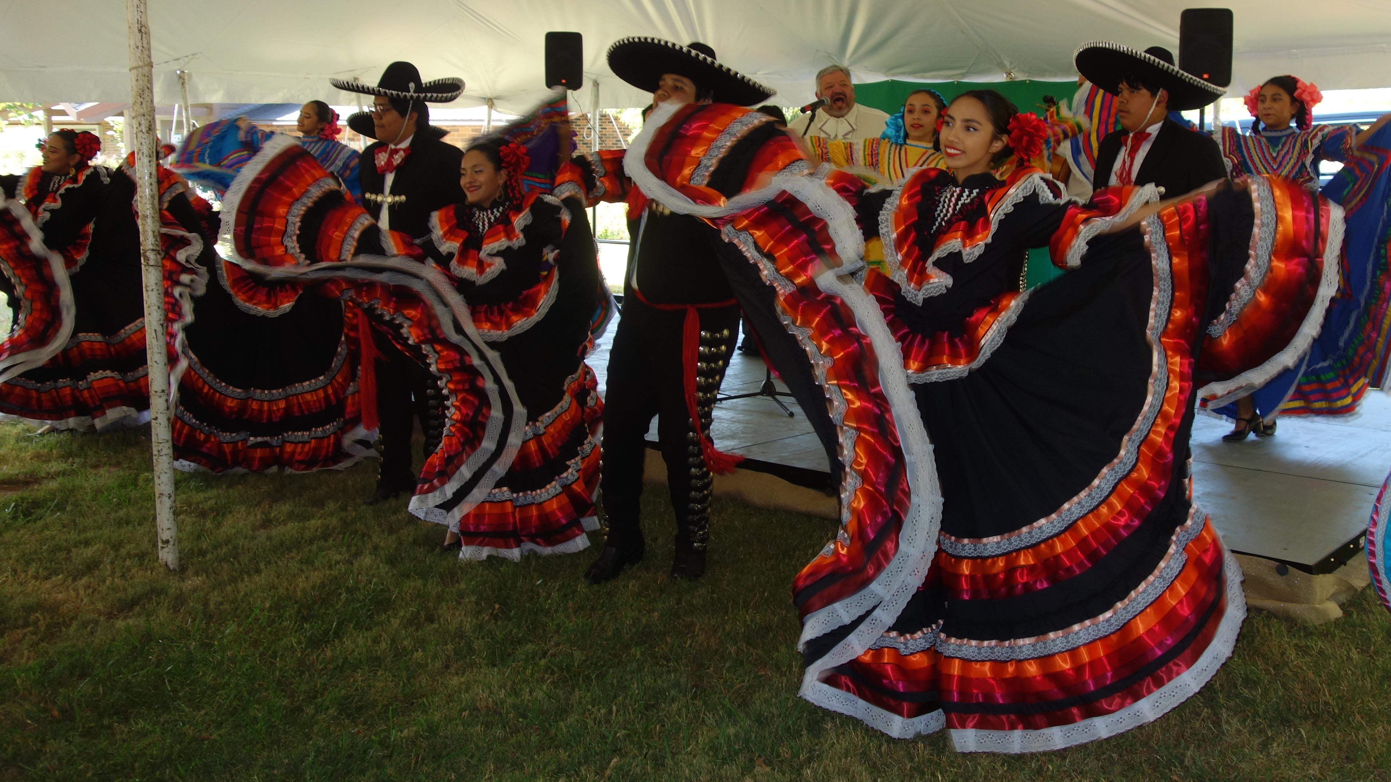 A group of men and women dancing in traditional clothing with live music. 