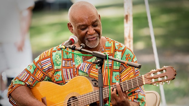 A man playing a guitar outside and signed. 