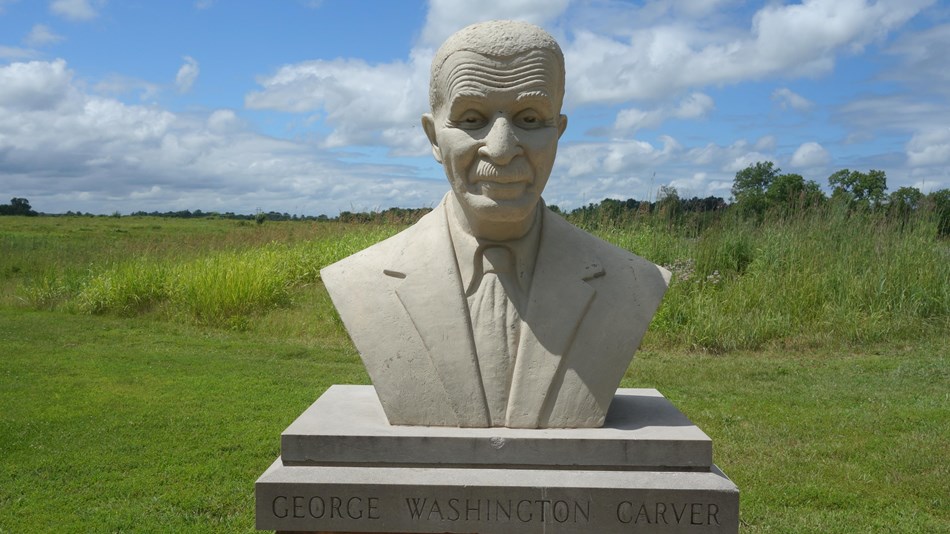 A cast concrete bust of George Washington Carver, depicted as an older man wearing a suit and tie.