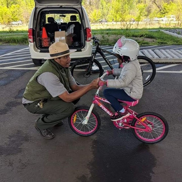 A ranger helps a child on a bike.