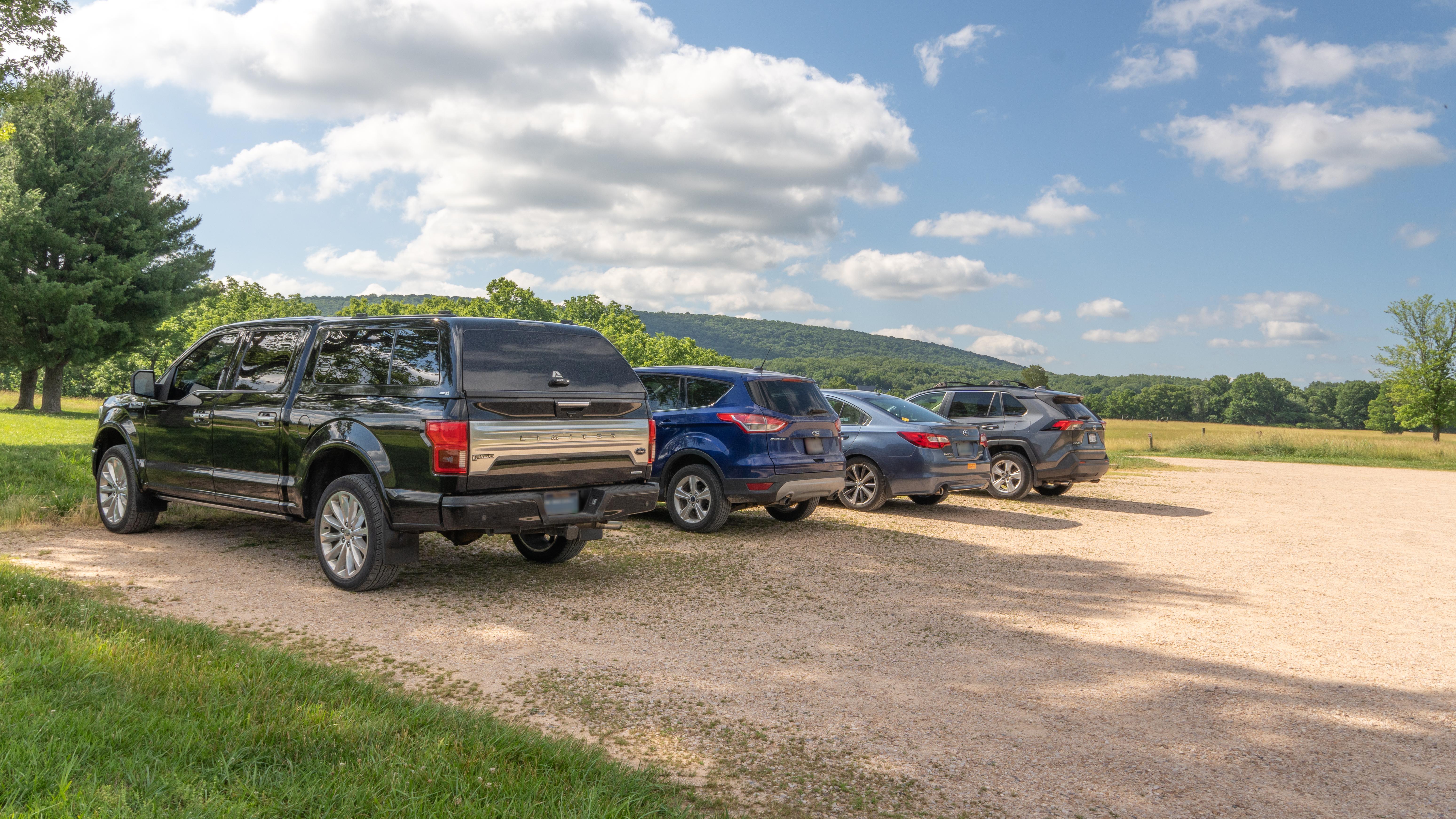 A row of cars parked in a gravel parking lot.