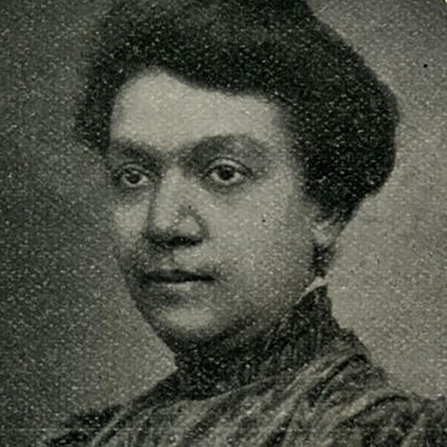 B/W historic portrait of a Black woman in a high collared dress with her hair in a bun