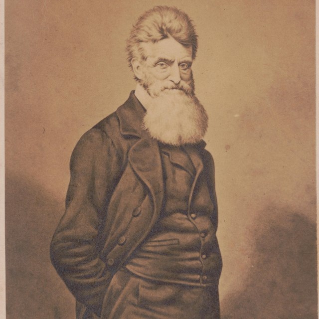 image of John Brown, wearing a vest and long coat, standing with his hands in his pants' pockets