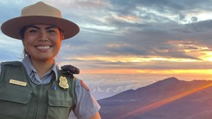 park ranger smiling at camera with sunrise over crater in background