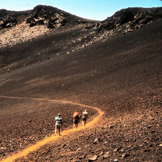 Three hikers walk along a trail with colorful cinder cones ahead of them.