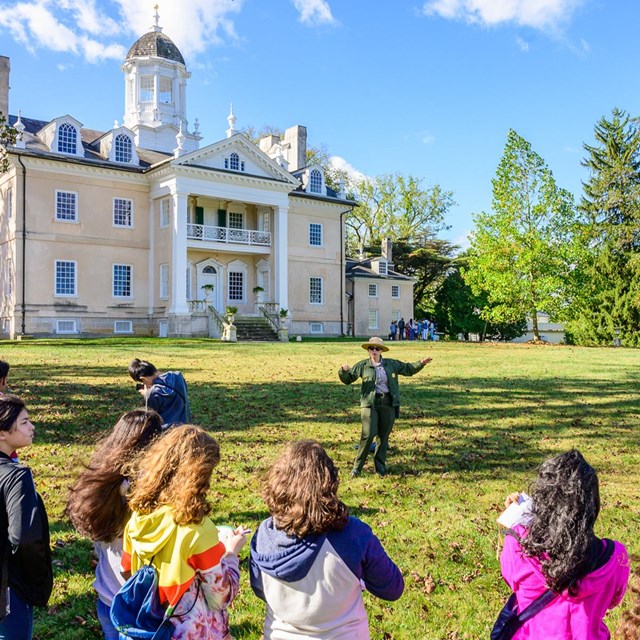 A ranger giving a talk to visitors in front of the mansion.