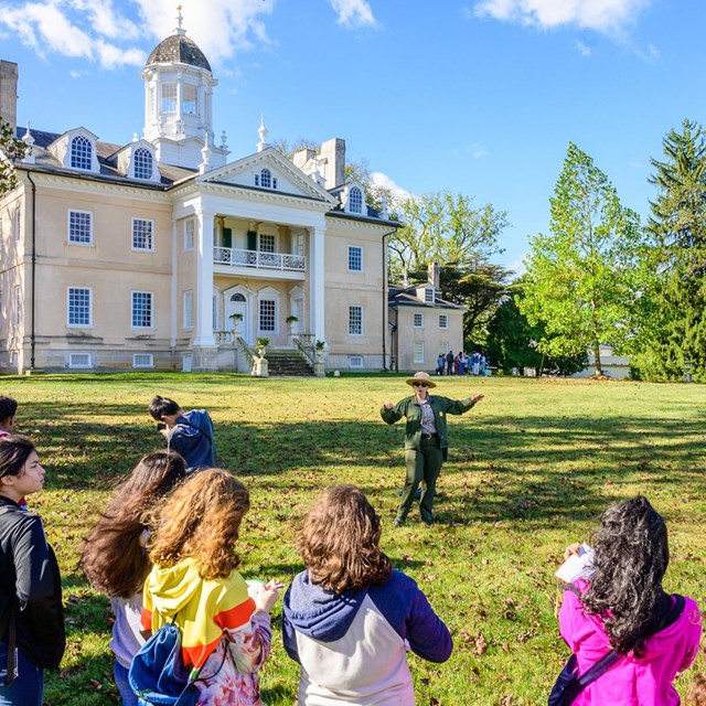 A ranger giving a talk to visitors in front of the mansion.