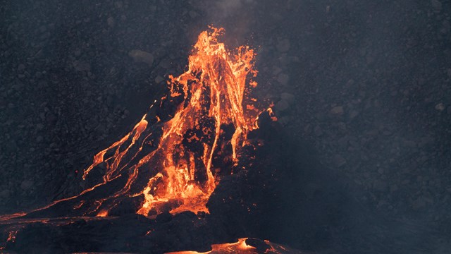 A volcanic cone spewing lava at night. 