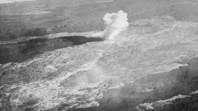 Black and white aerial photo of a bomb exploding on a lava flow