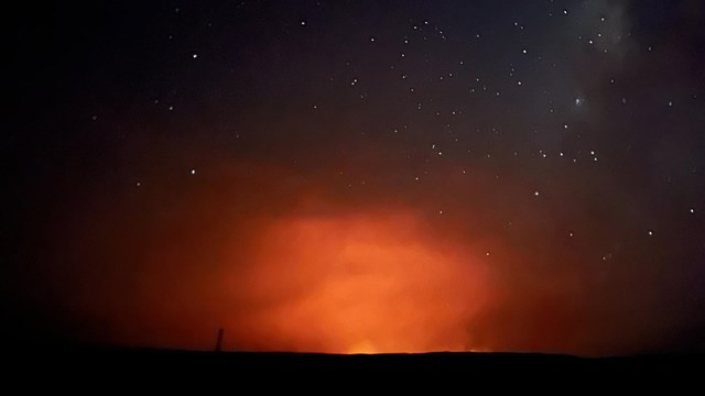 Bright red glow in distance amid dark night sky and stars.