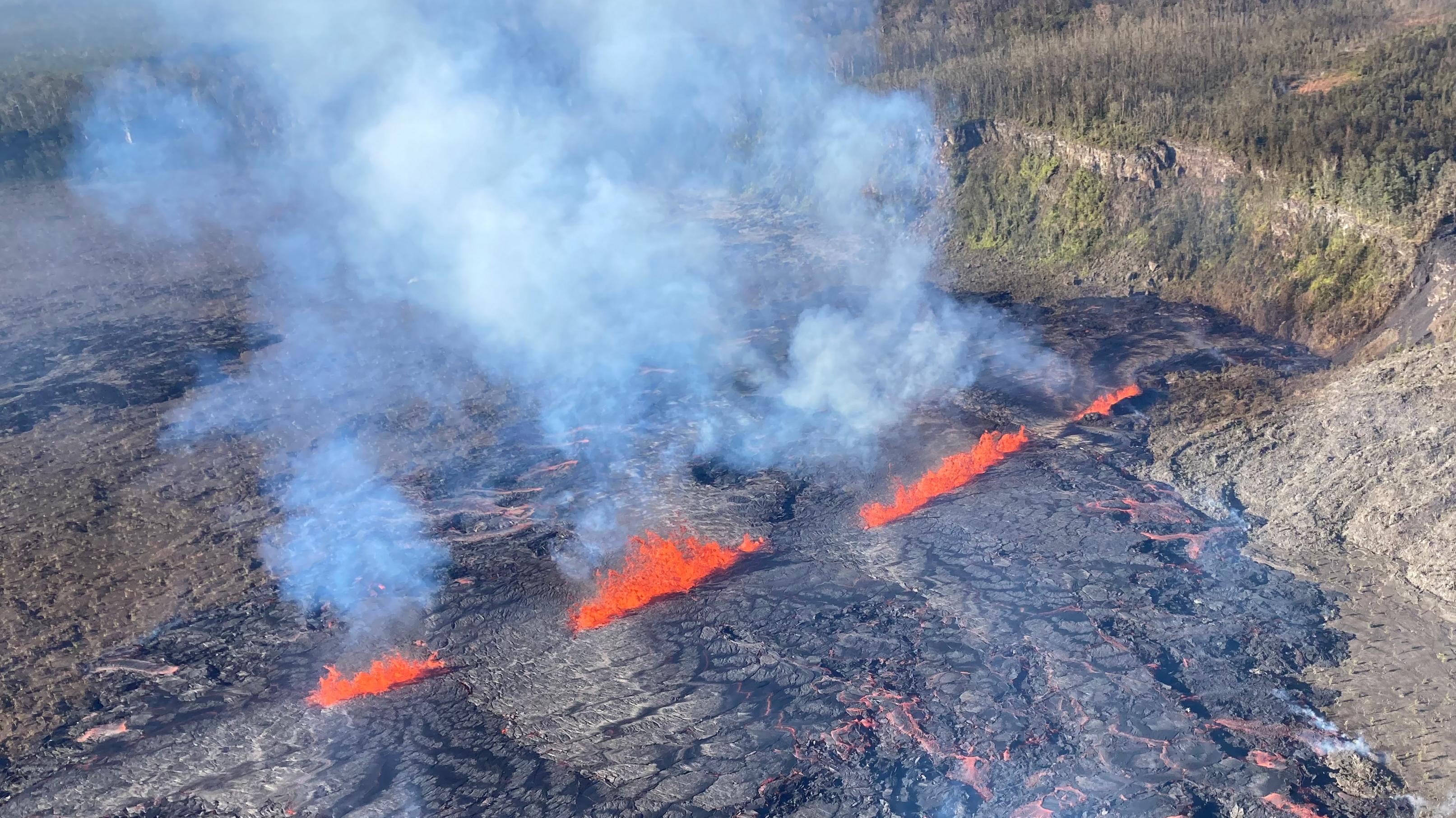 Line of bright red lava fissures inside a volcanic crater surrounded by green vegitation.