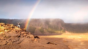 Rainbow inside a crater with a hiker in the foreground