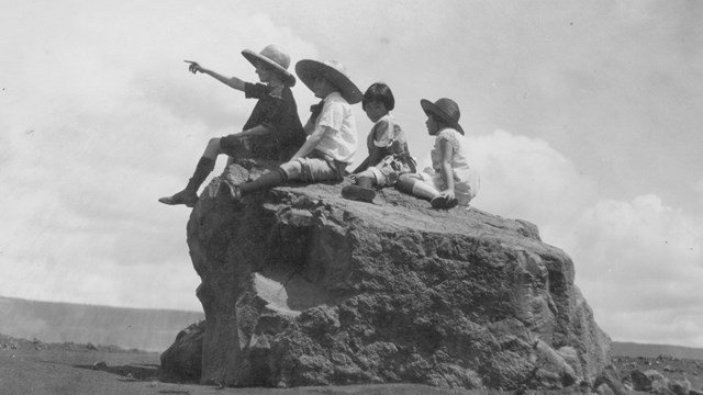 Historic photograph of four children sitting on an old ballistic in ash from the volcano.