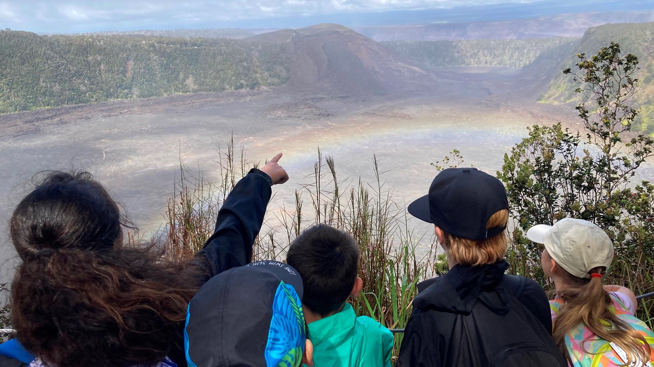 group of students point to rainbow above a volcanic crater