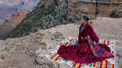 woman sits on colorful blanket on a cliff overlooking canyons