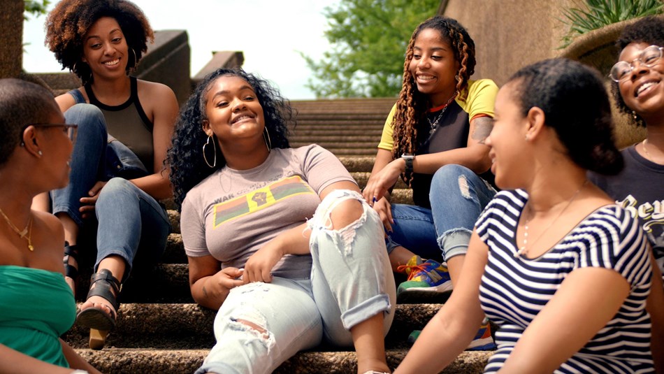 young women sit on steps in a park while laughing and talking