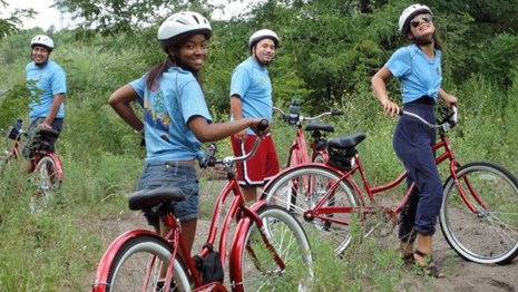 Young adults standing with red bikes and wearing helmets