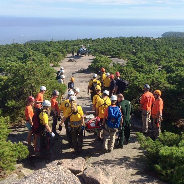 Search and Rescue volunteers carry a visitor on a stretcher to a helicopter