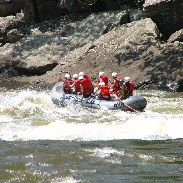 Group of paddlers wearing helmets and life jackets in inflatable raft on river