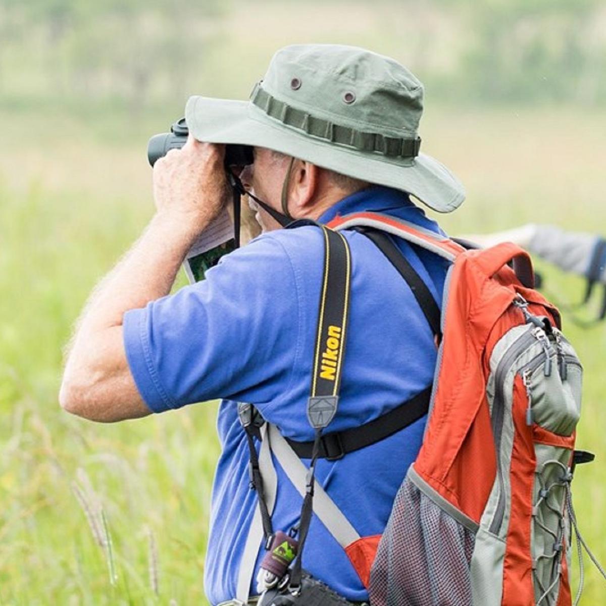 Man looking through binoculars and group of people pointing in background