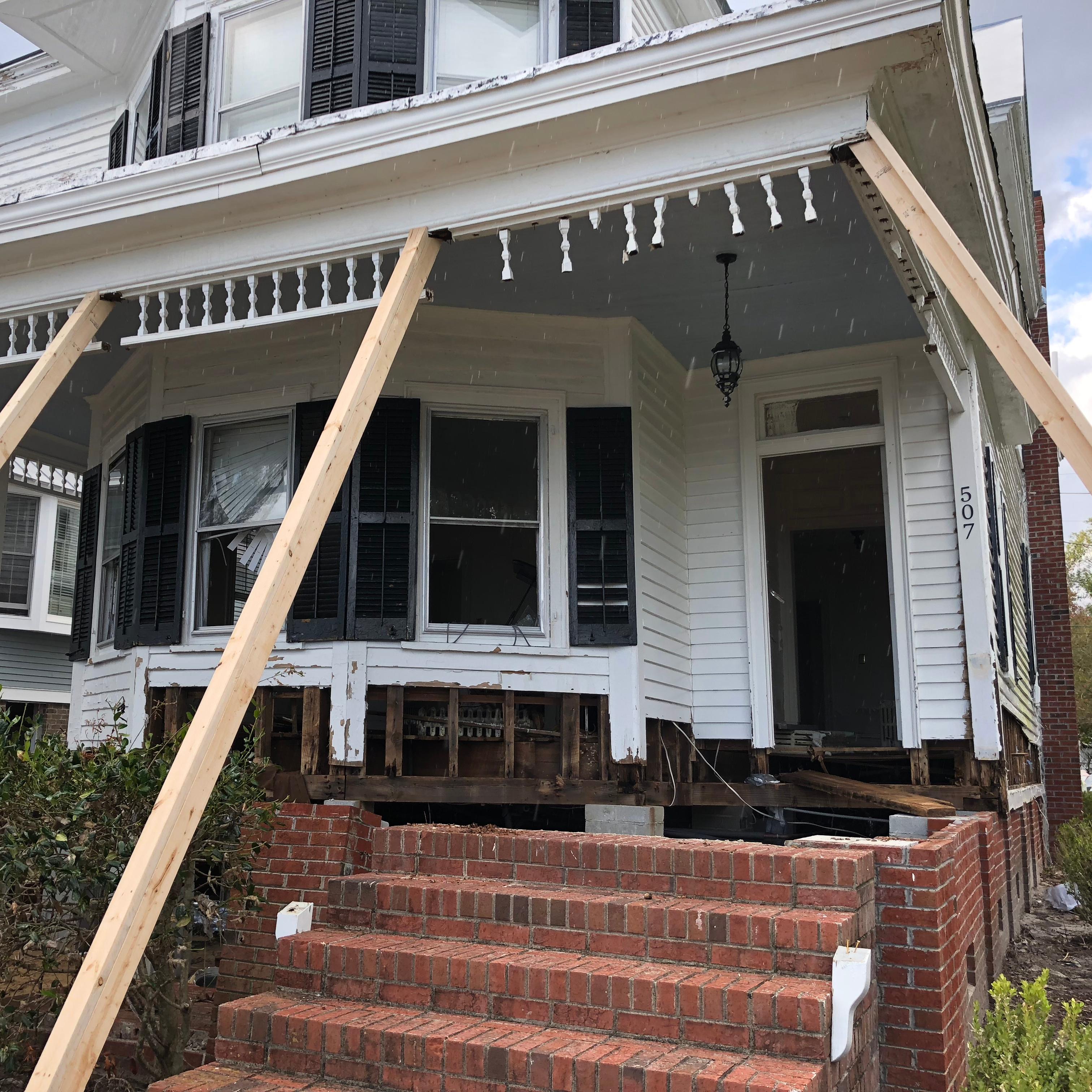 White frame home with porch roof supported by temporary shoring.