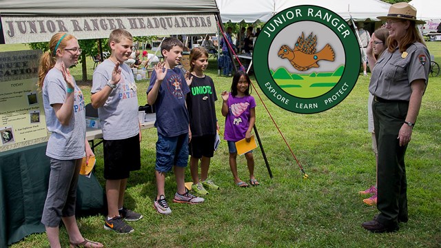 Kids with their left hand raised listen to a ranger speak