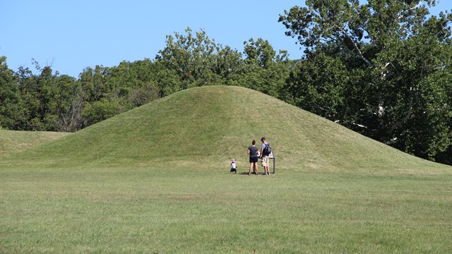 Three people stand in front of a grass-covered mound
