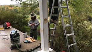 Two park rangers repair a wooden porch.