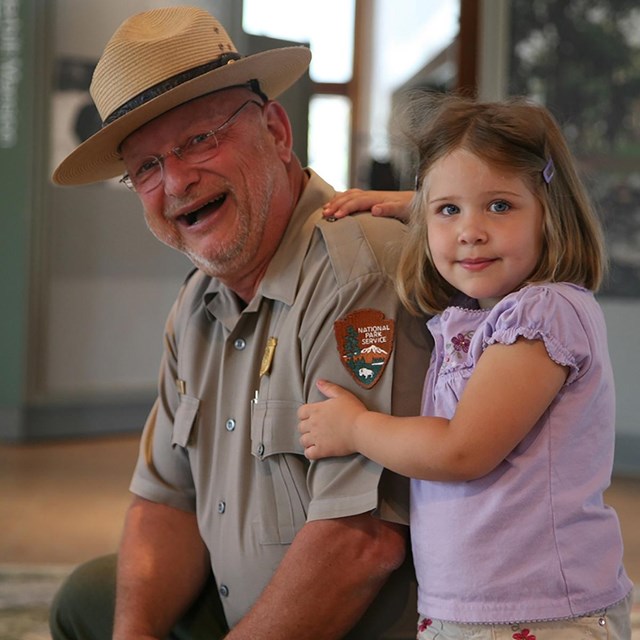 A park ranger with a young girl smiles at the camera.