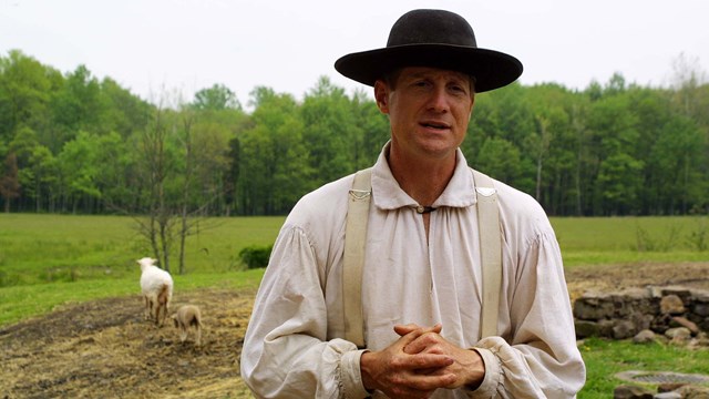 Man in white shirt and black hat stands in barnyard.