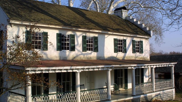 Front of a white building with green shutters and a porch. 