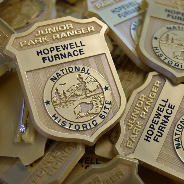 Pile of gold junior ranger pins that say Hopewell Furnace National Historic Site