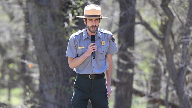Park ranger in uniform speaks to audience at an outdoor event.
