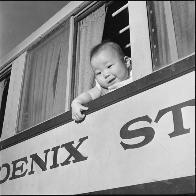A baby leans out a window on the day residents leave Poston