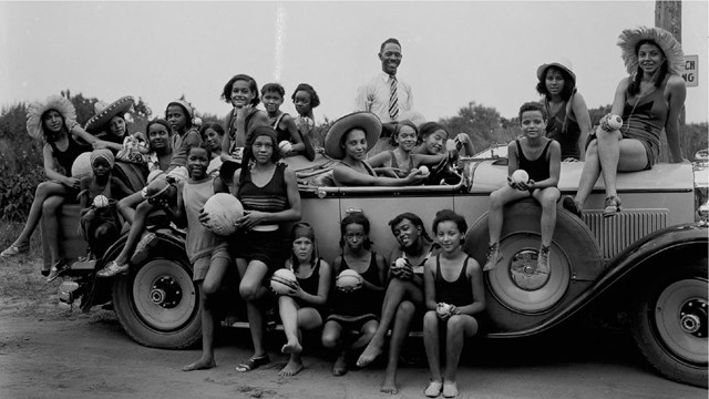 22 African American boys and girls sit around a light colored convertable wearing bathing suits