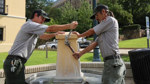 Two maintenance workers fixing a jug fountain in the park