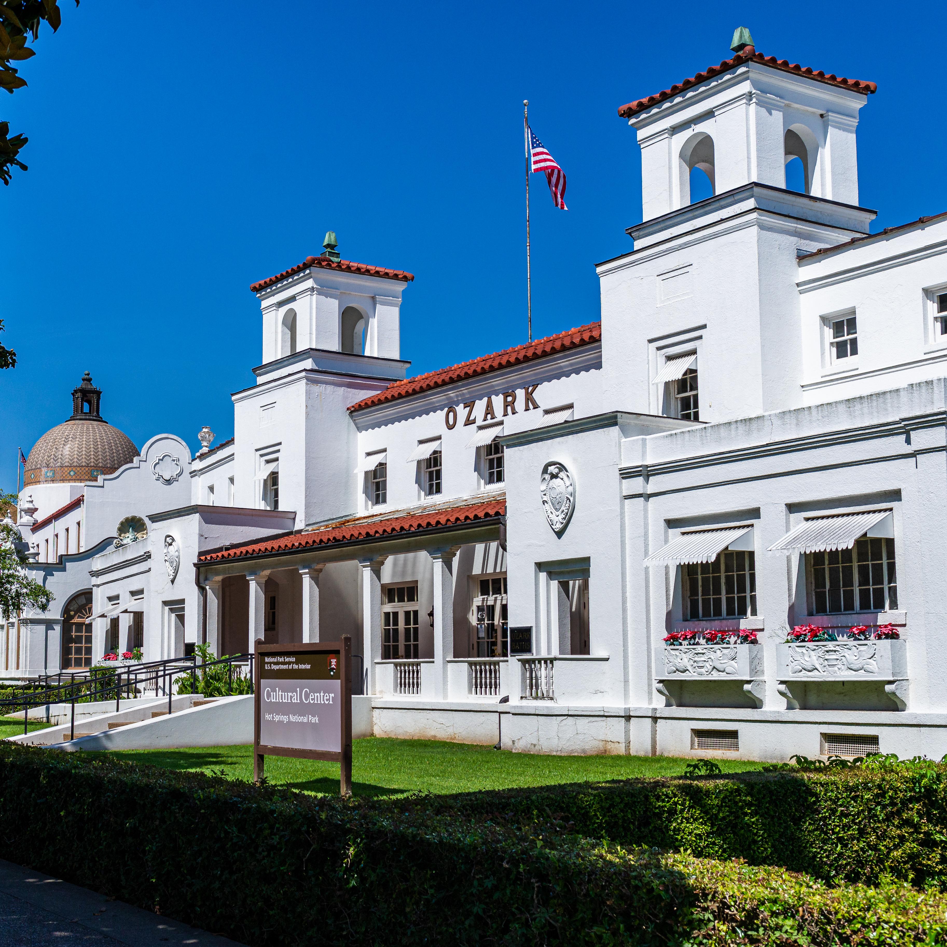 An active scene in front of the Fordyce Bathhouse; people sitting ,walking, and looking joyous.