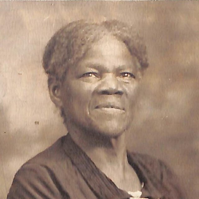 An African American woman with gray hair wears a dark shirt with two white stripes