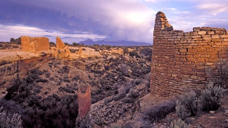 remains of stone structures around a canyon, purple sky behind
